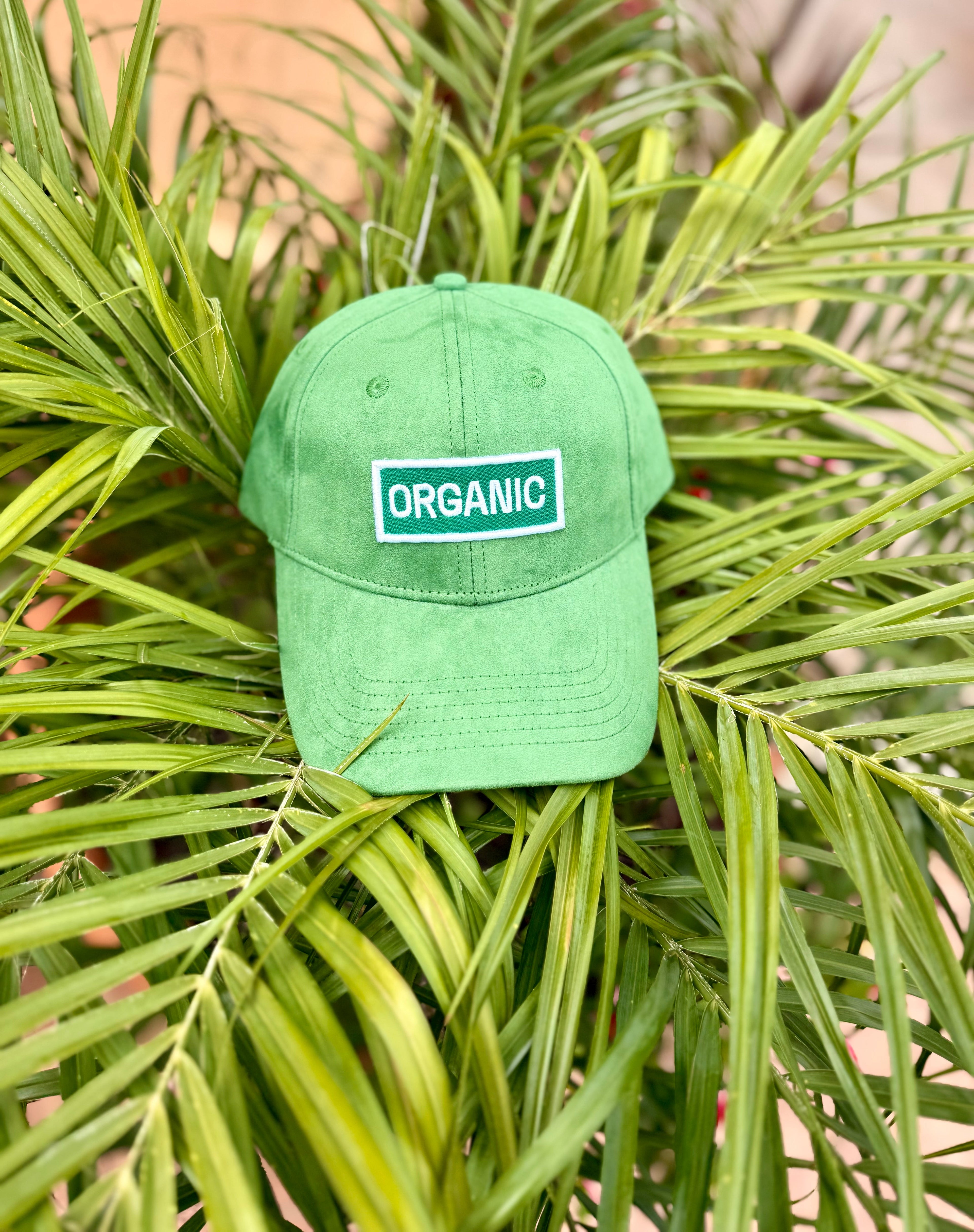 Front view of bABP "ORGANIC" green eco-suede signature hat with white logo patch, displayed against lush green tropical leaves