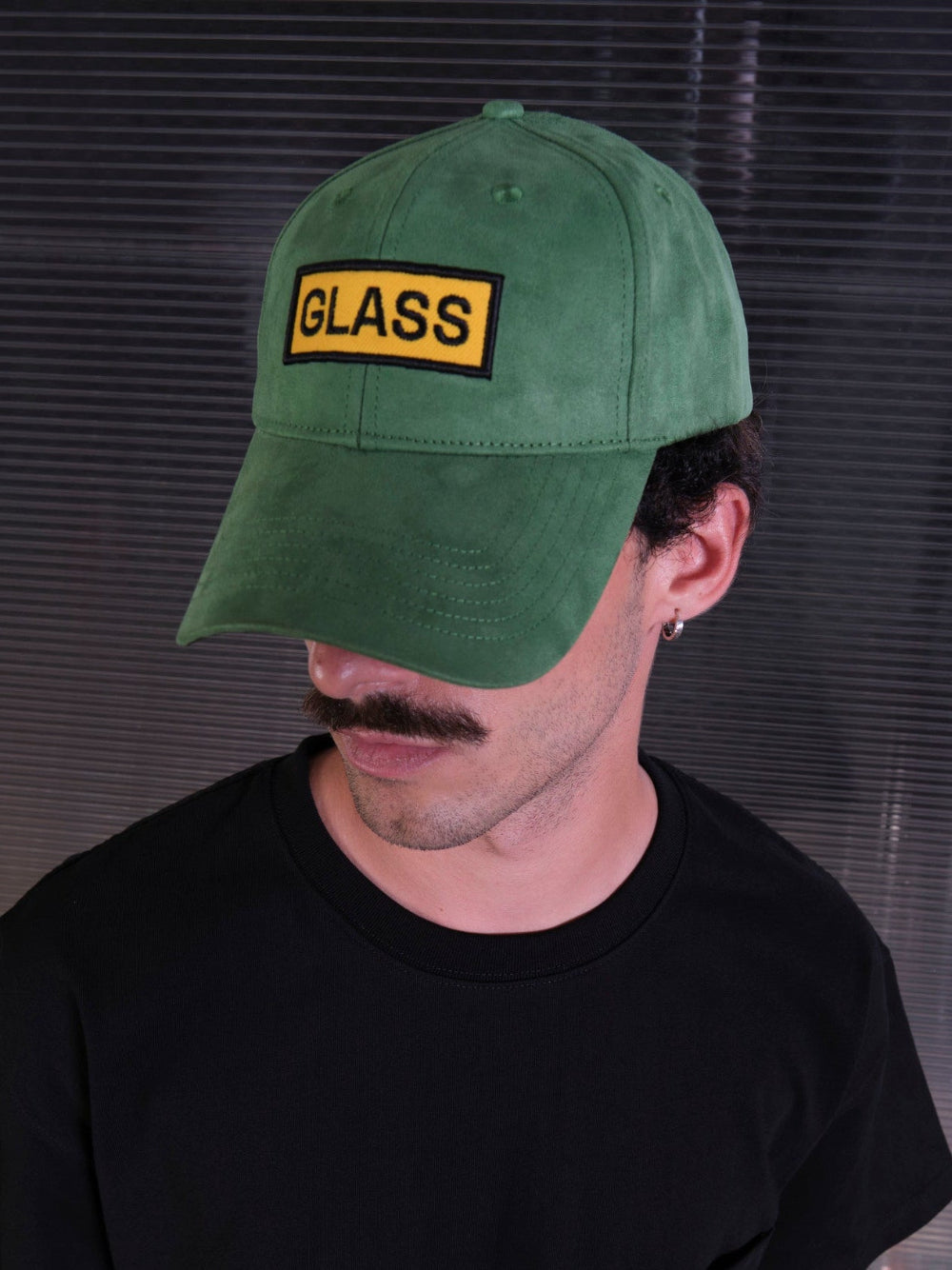 bABP Glass green eco-suede hat from the Signature Collection, cropped portrait view of a model in a black t-shirt, focusing on the green hat and yellow "GLASS" logo patch