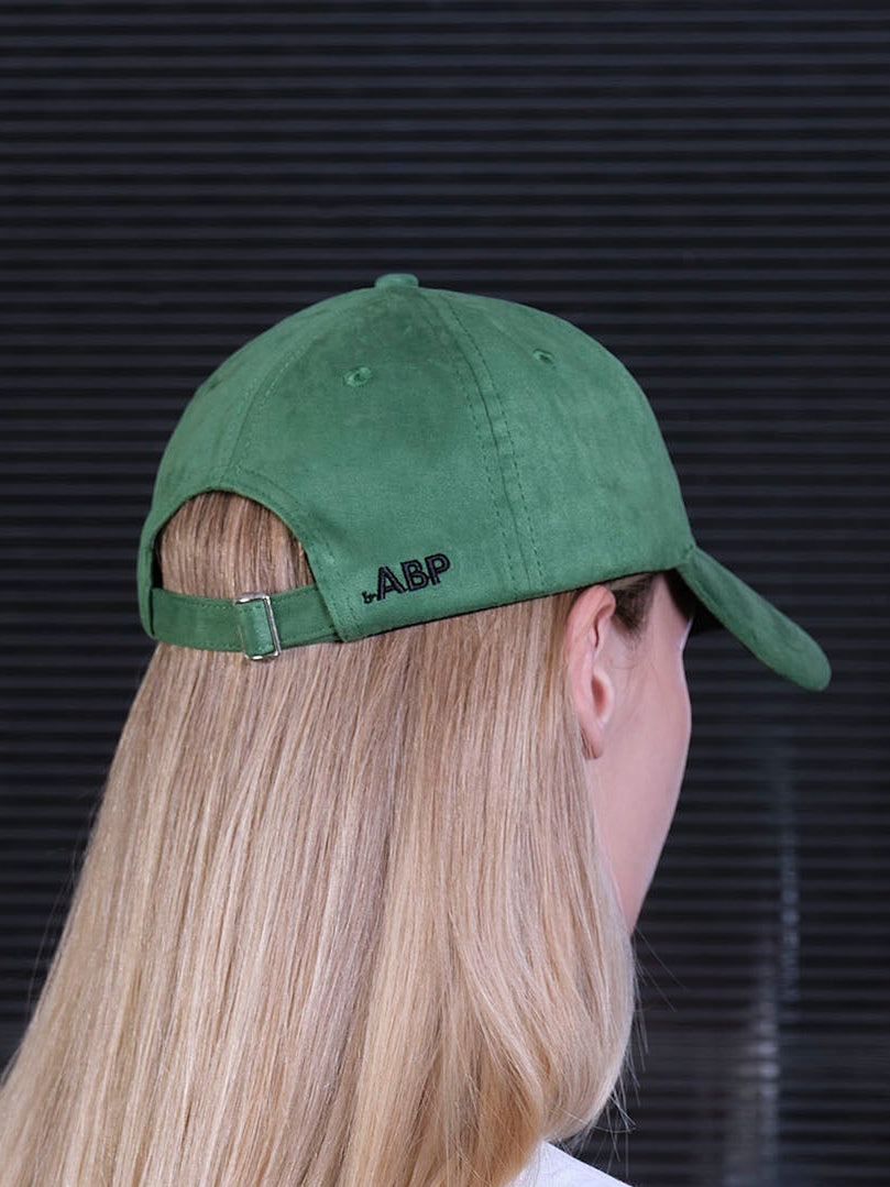 bABP green eco-suede hat from the Signature Collection, back view on a female model with long blonde hair showing the adjustable strap and bABP logo