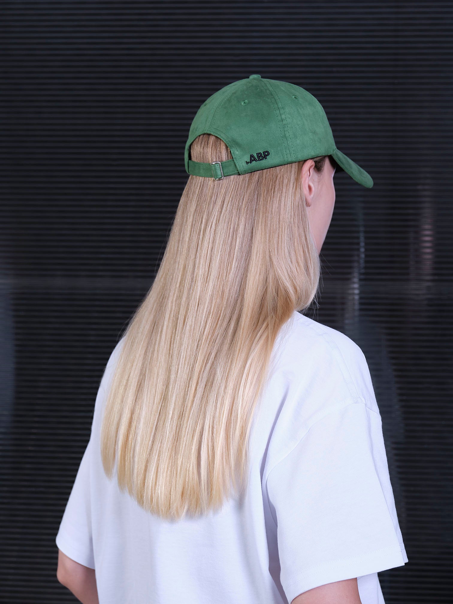 bABP green eco-suede hat from the Signature Collection, back view on a model with long blonde hair, showing the adjustable strap and embroidered bABP logo