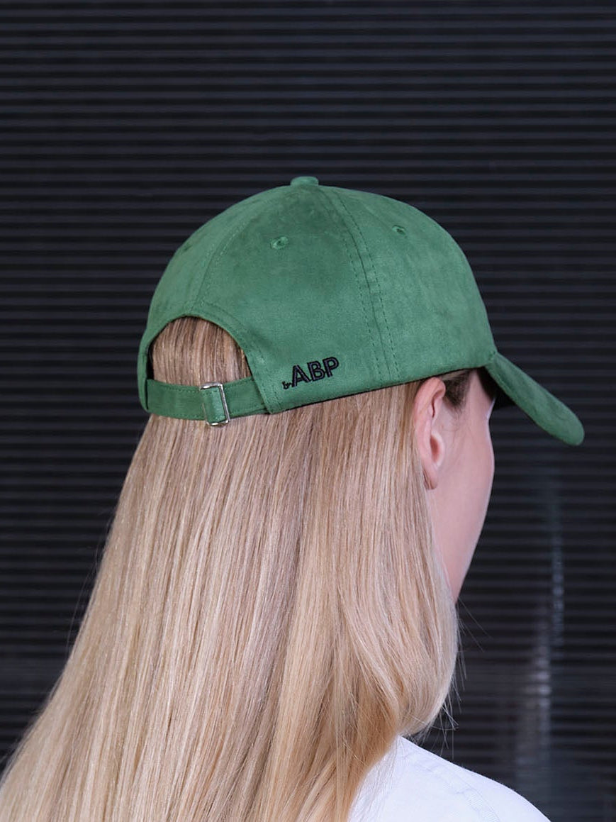 bABP green eco-suede hat from the Signature Collection, back view on a model with long blonde hair, showing the adjustable strap and embroidered bABP logo