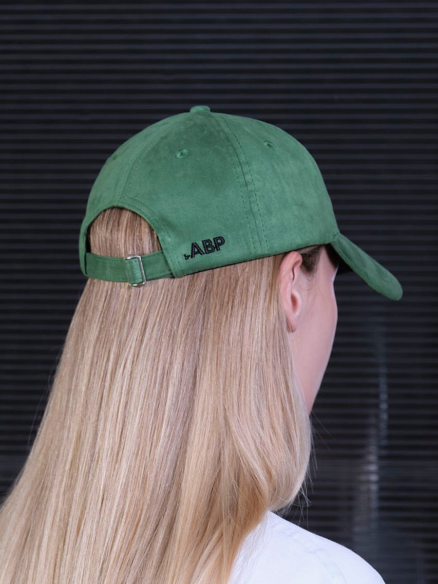 bABP green eco-suede hat from the Signature Collection, back view on a female model with long blonde hair, showing the adjustable strap and bABP logo