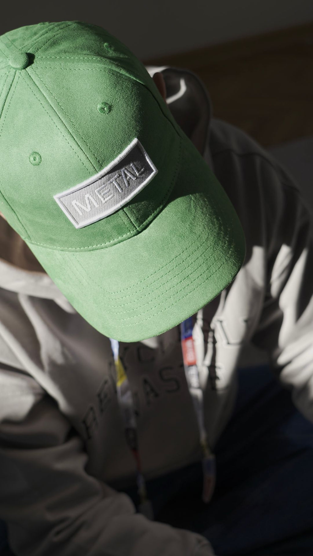 bABP Metal green eco-suede hat from the Signature Collection, portrait view of a model in a gray "Recyclable" hoodie, highlighting the silver-toned "METAL" logo patch