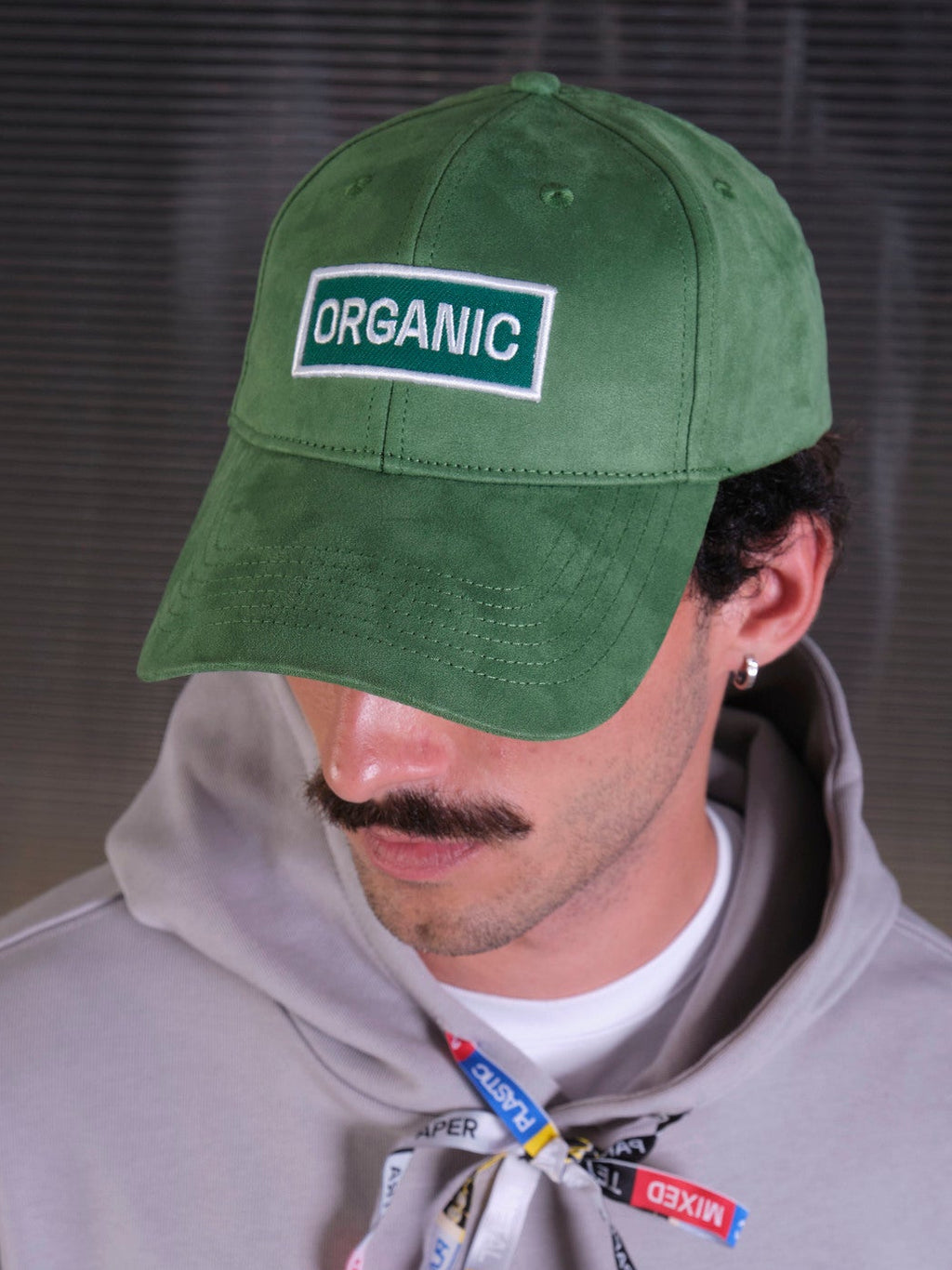 bABP Organic green eco-suede hat from the Signature Collection, close-up portrait view of a model with a mustache wearing a gray hoodie, highlighting the white "ORGANIC" logo patch