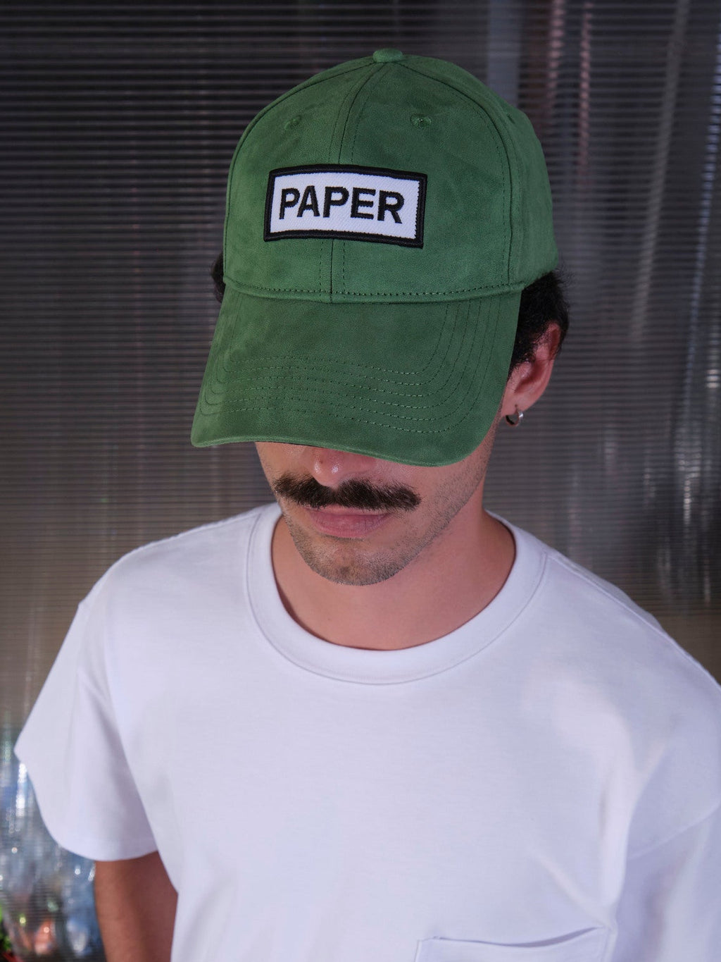 bABP Paper green eco-suede hat from the Signature Collection, portrait view of a model with a mustache, highlighting the white "PAPER" logo patch and premium texture