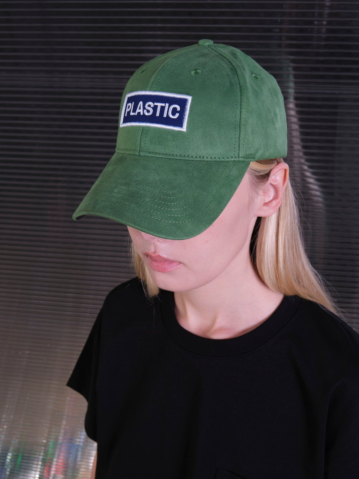 bABP Plastic green eco-suede hat from the Signature Collection, portrait view of a female model with blonde hair, highlighting the white "PLASTIC" logo patch