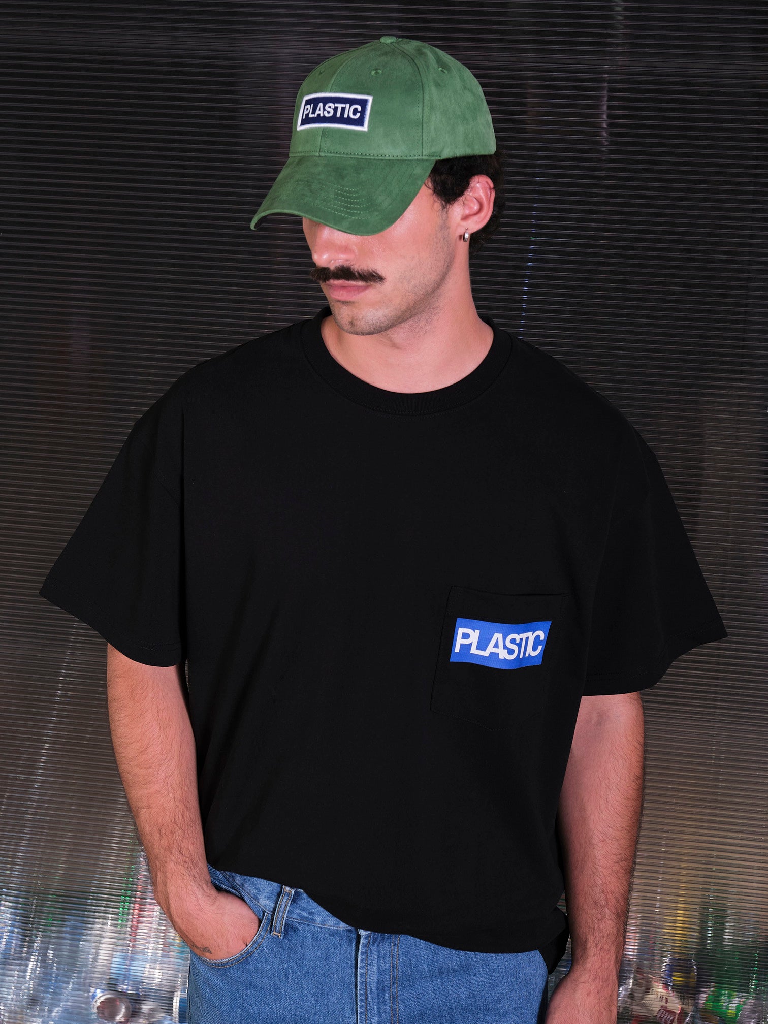 bABP Plastic green eco-suede hat from the Signature Collection, portrait view of a model with a mustache in a black pocket tee, highlighting the white "PLASTIC" logo patch and premium texture
