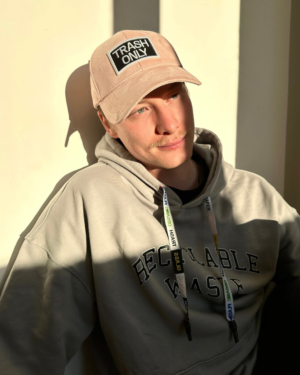 bABP Trash Only light pink eco-suede hat from the Signature Collection, portrait view of a model in a gray hoodie, showcasing the premium pink fabric and embroidered patch