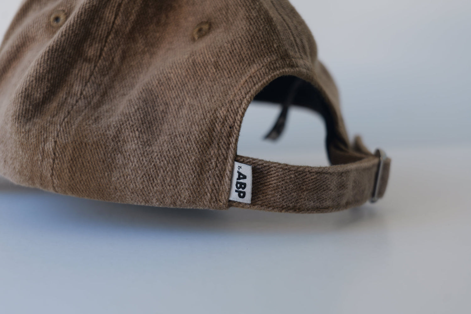 Close-up view of the back of the bABP B-SIDE brown washed cotton hat showing the adjustable strap with a metal buckle and the signature white "bABP" woven logo tag