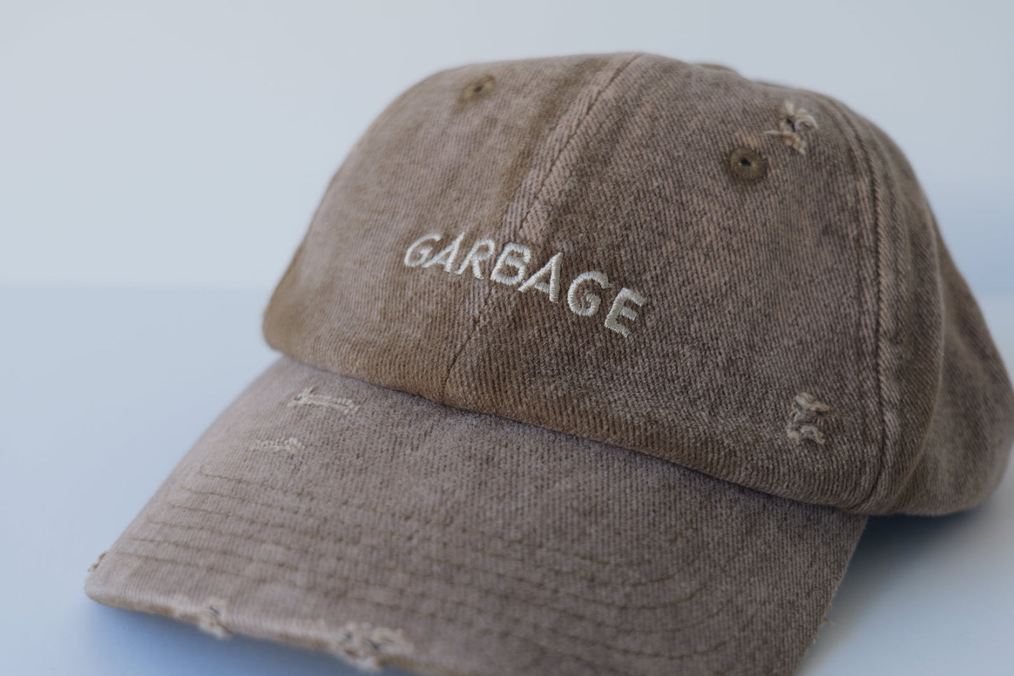 Front studio view of the bABP B-SIDE brown washed cotton hat with "GARBAGE" embroidered in a matching light tan thread and heavy distressed details