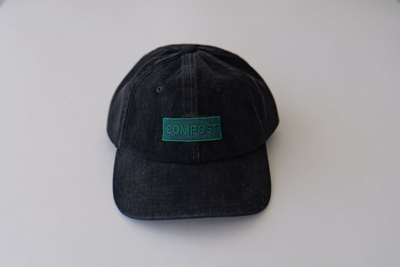 Side studio profile of the bABP B-SIDE "COMPOST" black washed cotton hat featuring a vibrant green embroidered logo patch on a light gray background