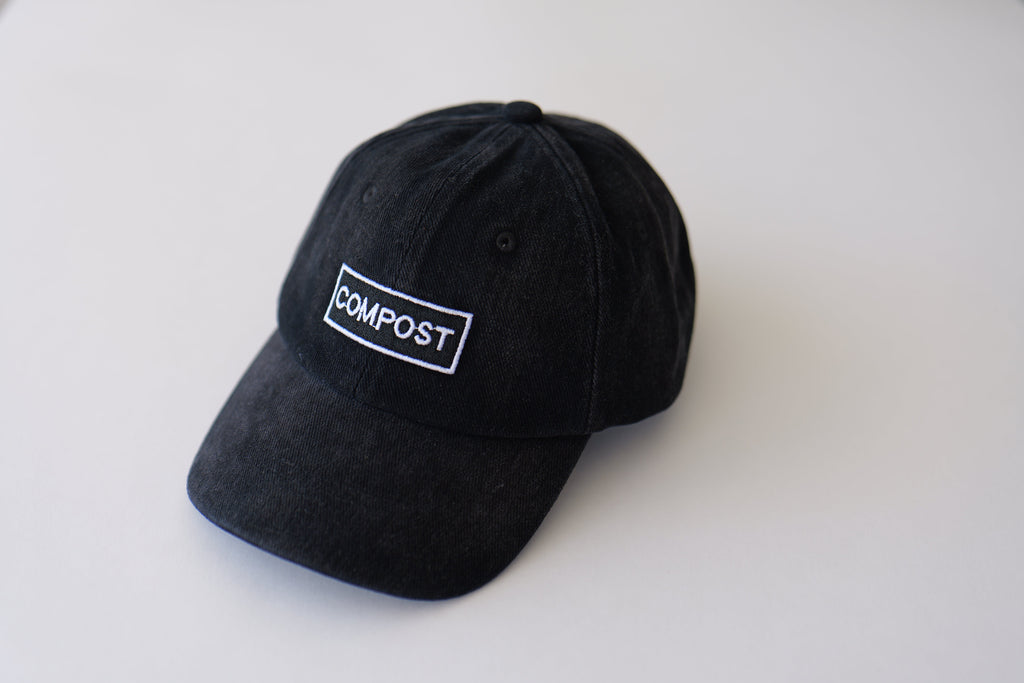 Front angled studio shot of the bABP B-SIDE "COMPOST" black washed cotton hat with a high-contrast white logo patch on a clean light gray background