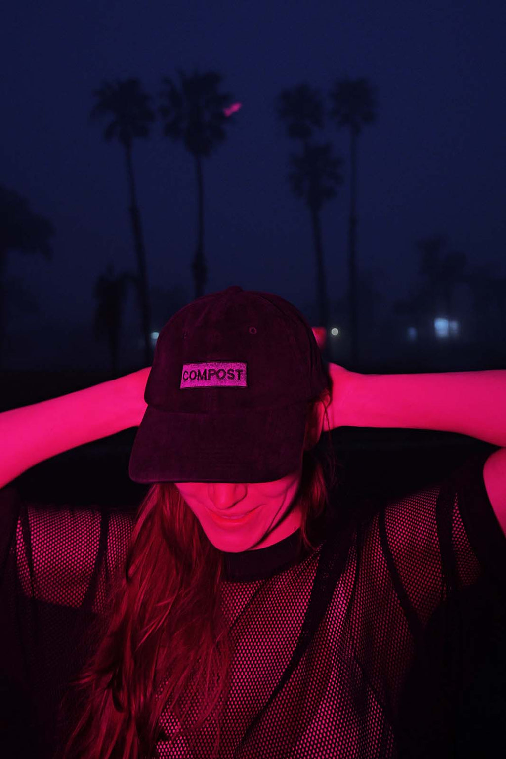 Lifestyle photo of a person wearing the bABP B-SIDE black washed cotton "COMPOST" hat at night with palm trees and pink neon lighting, urban streetwear vibe