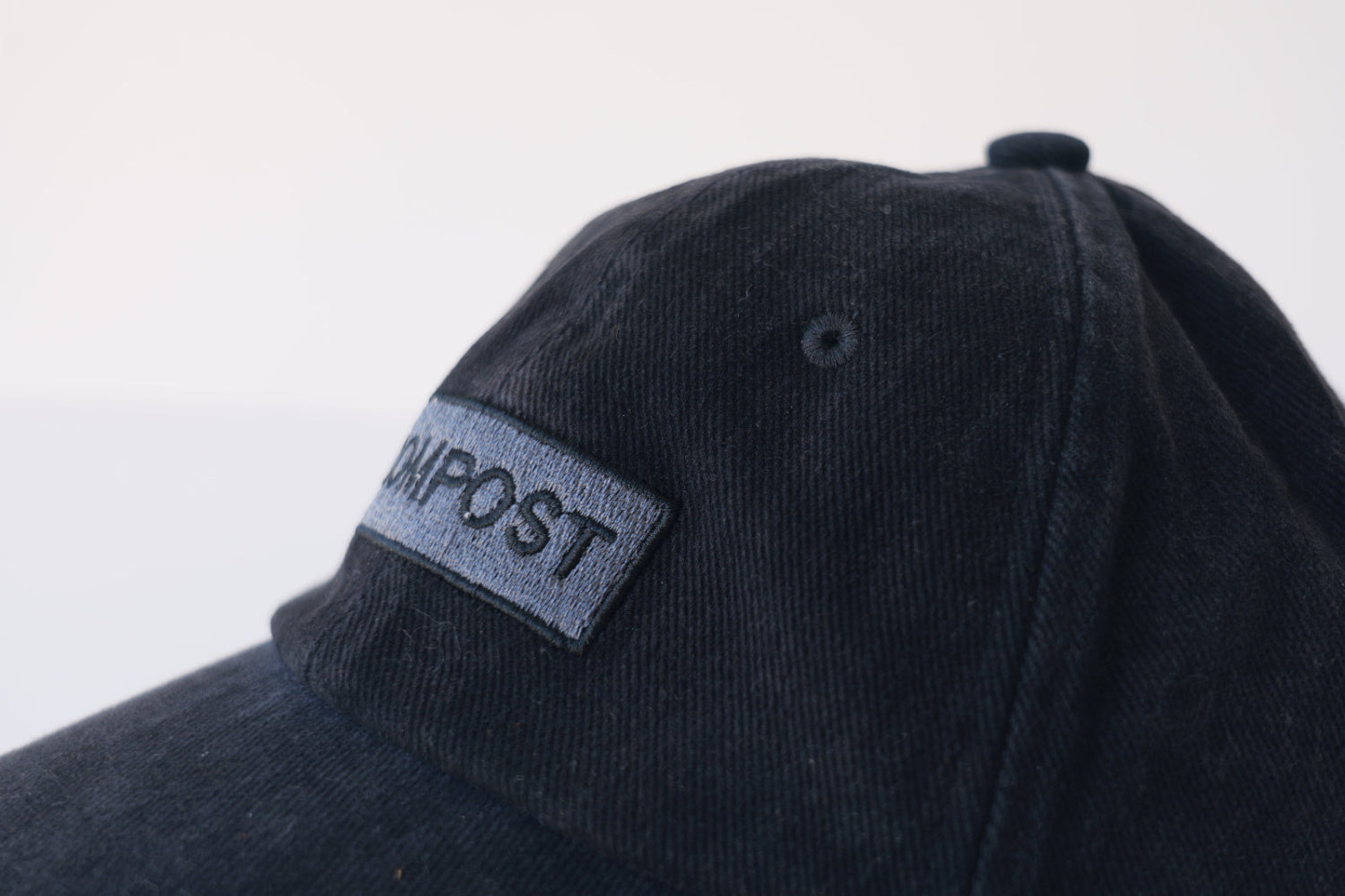 Extreme close-up of the bABP B-SIDE black washed cotton hat featuring a gray embroidered "COMPOST" logo patch and heavy washed fabric texture