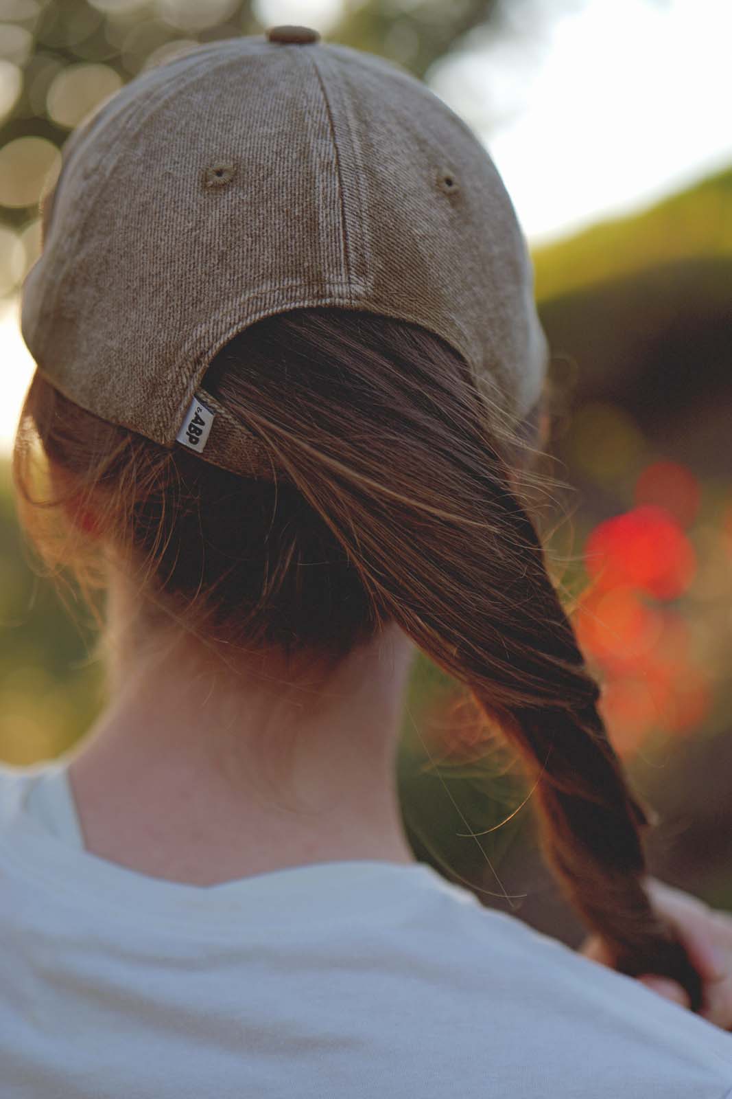 Back view of a person with a long ponytail wearing the bABP B-SIDE tan washed cotton hat, showing the adjustable strap and white "bABP" logo label