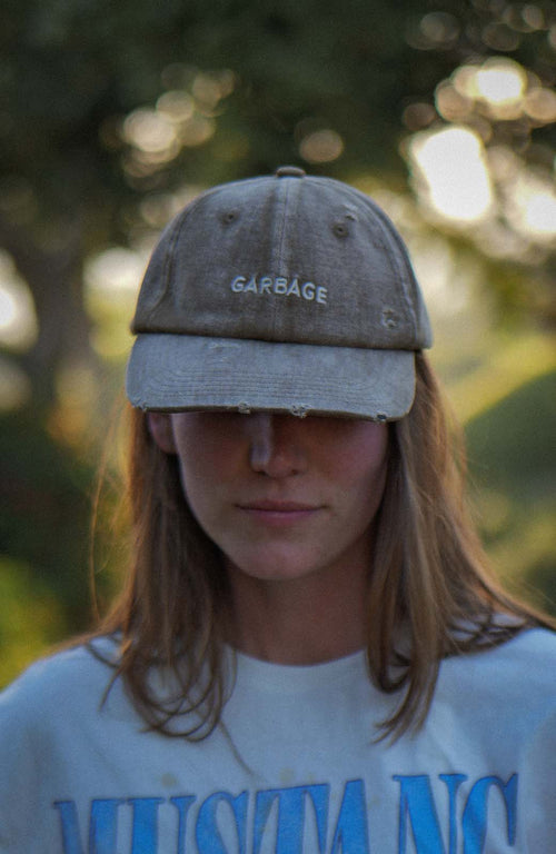Front lifestyle view of a person wearing the bABP B-SIDE tan washed cotton hat with "GARBAGE" embroidery, paired with a vintage Mustang t-shirt