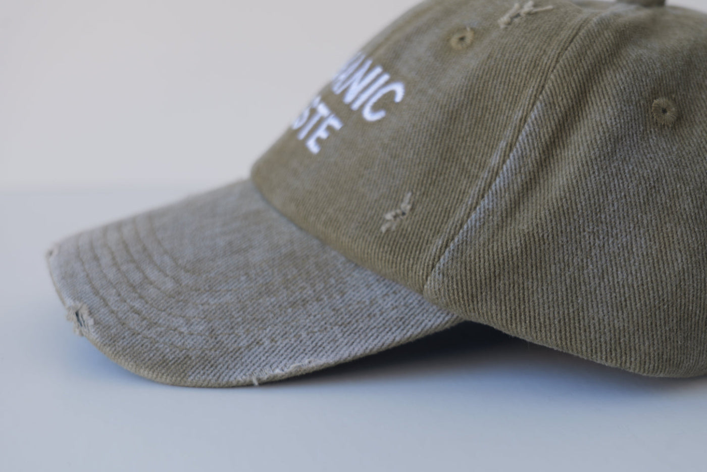 Left side profile view of the bABP B-SIDE olive washed cotton hat featuring "ORGANIC WASTE" white embroidery and authentic distressed details on a light gray background