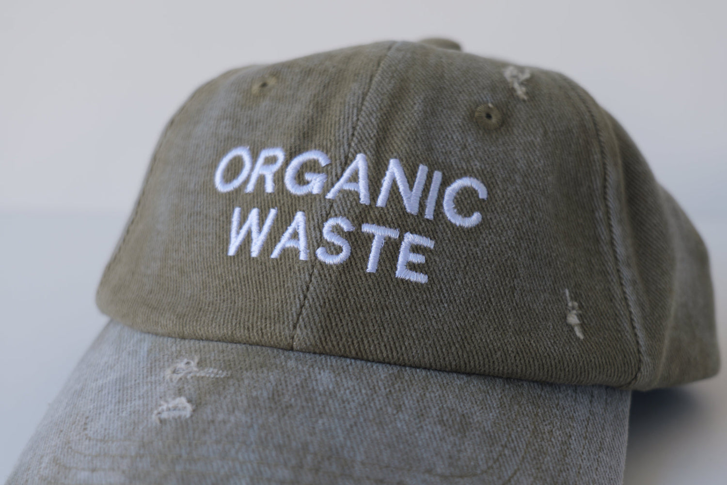 Front angled view of the bABP B-SIDE olive washed cotton hat featuring white "ORGANIC WASTE" embroidery and distressed details, part of the Street Approved Goods series