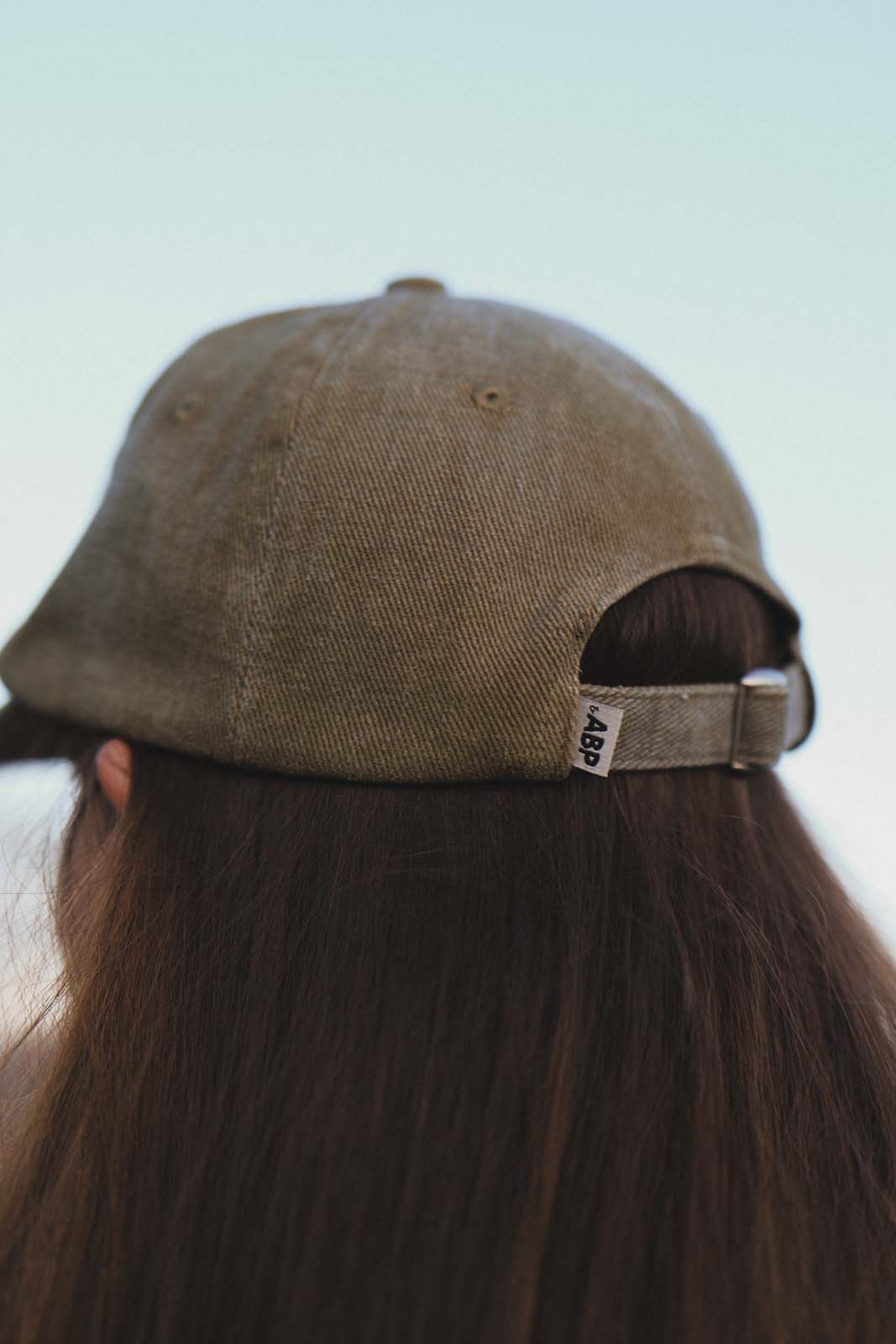 Close-up back view of a person wearing the bABP B-SIDE olive washed cotton hat, showing the adjustable strap with metal buckle and white "bABP" side logo label