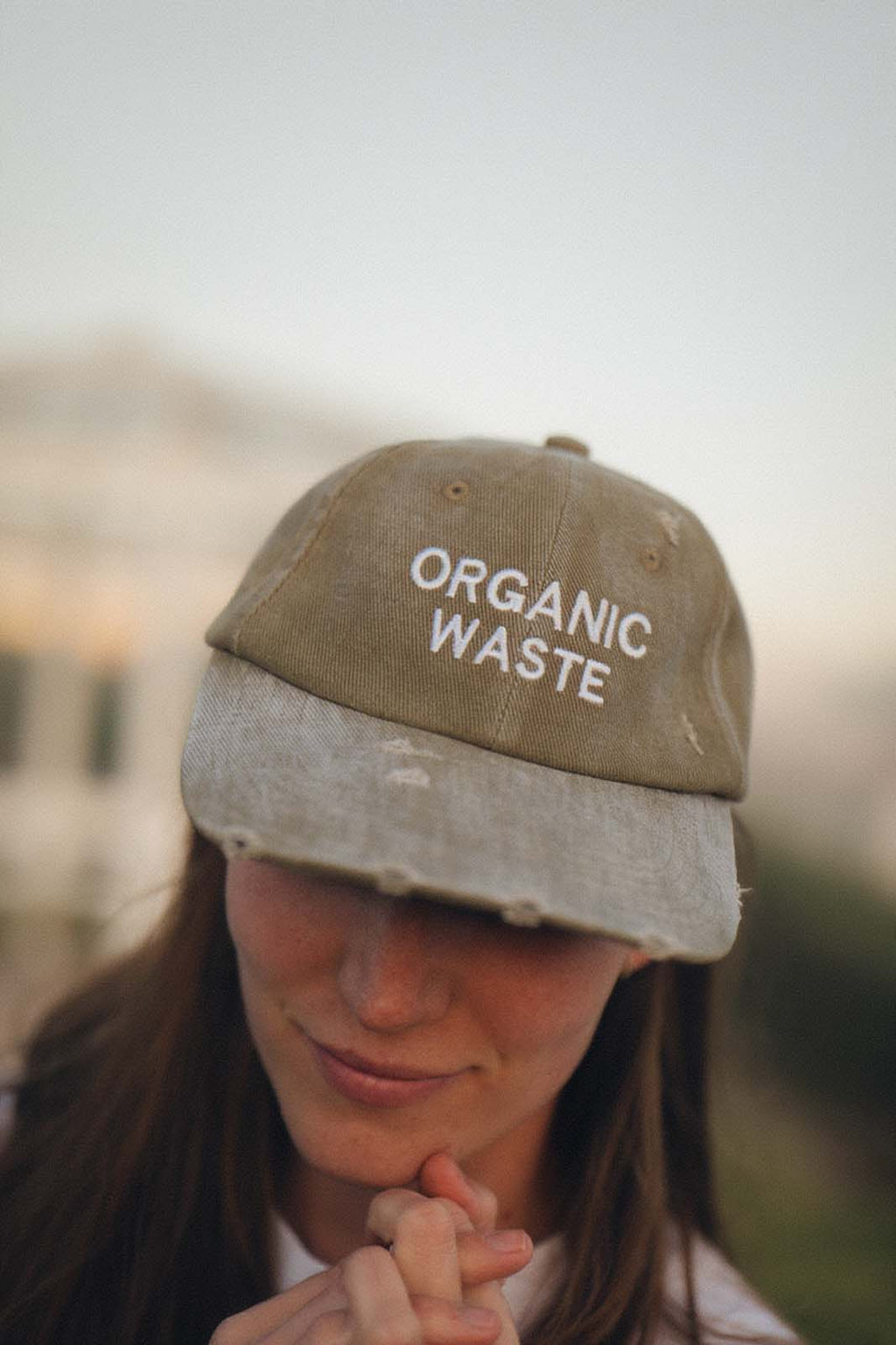 Close-up lifestyle view of a person wearing the bABP B-SIDE olive washed cotton hat with "ORGANIC WASTE" embroidery and distressed brim details