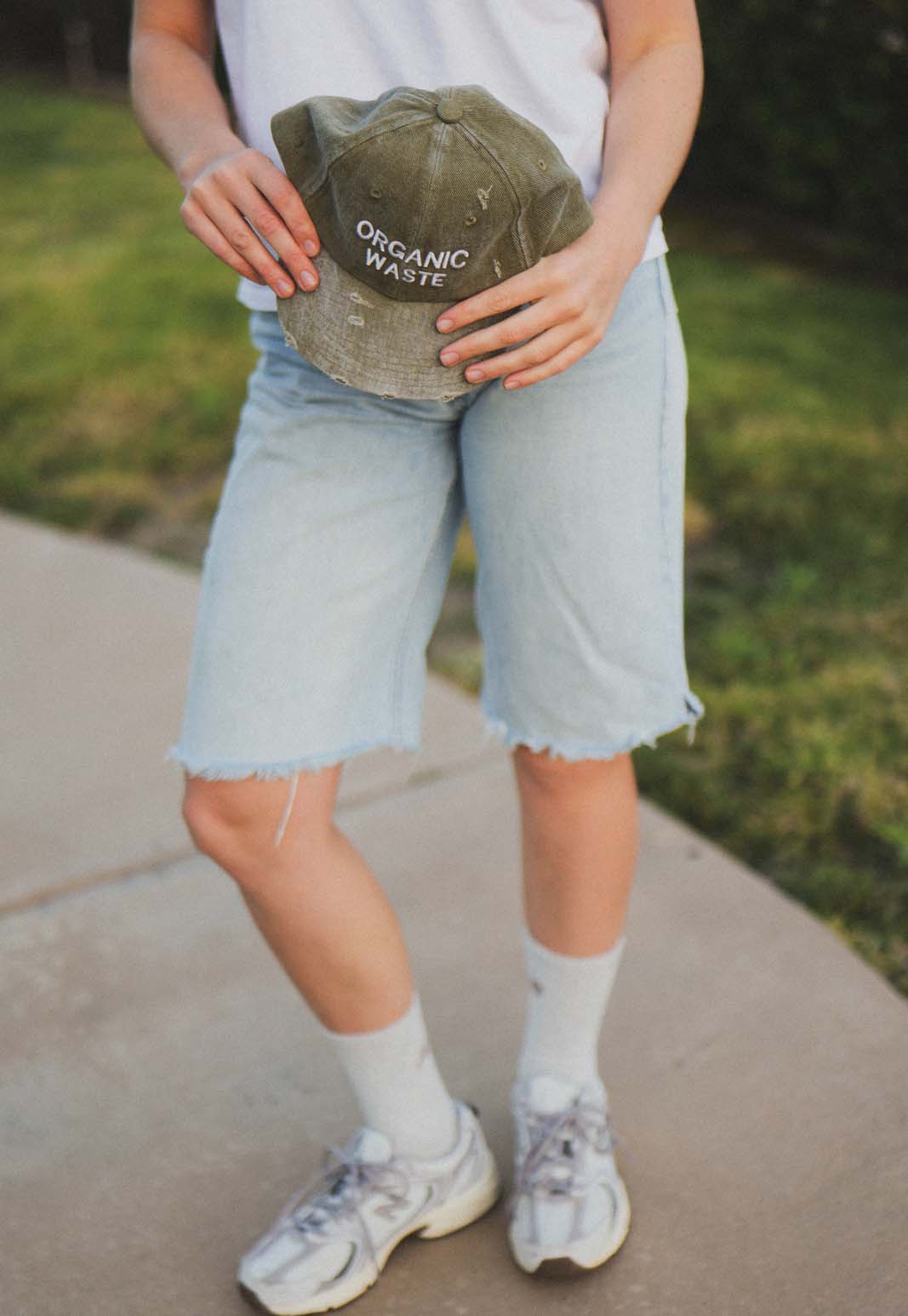 Lifestyle view of a person holding the bABP B-SIDE olive washed cotton hat with white "ORGANIC WASTE" embroidery, featuring a distressed streetwear aesthetic