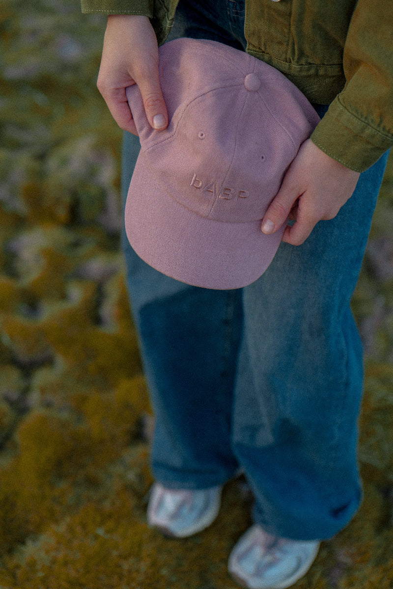 Close-up of bABP B-SIDE pink cotton hat with tonal embroidered logo, held by model in an outdoor setting, premium washed texture detail