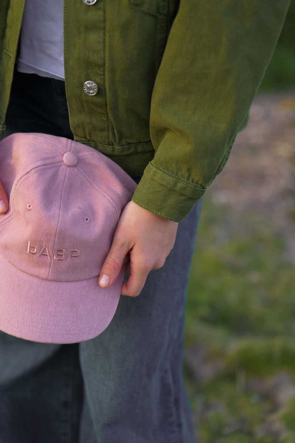 Close-up of the bABP B-SIDE pink heavy cotton hat held in hand, showing the tonal "bABP" logo embroidery and the rugged fabric texture against a green utility jacket