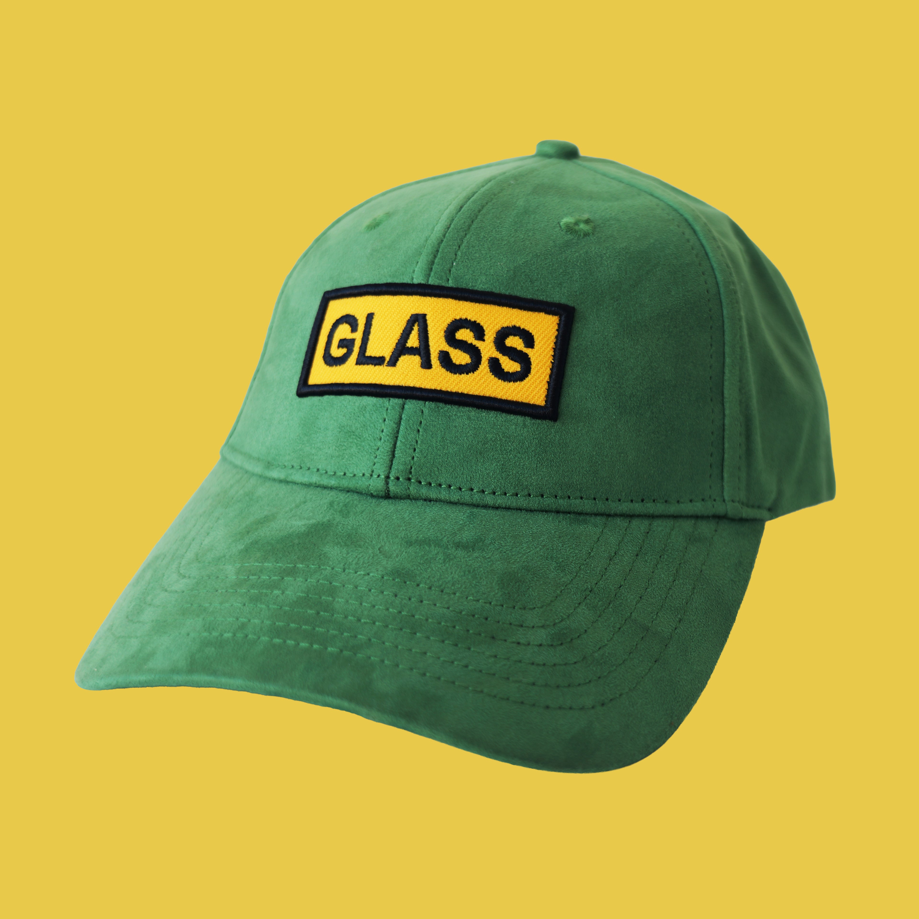 Professional studio shot of bABP "GLASS" green eco-suede hat with a yellow and black embroidered logo patch, featured on a matching monochromatic yellow background