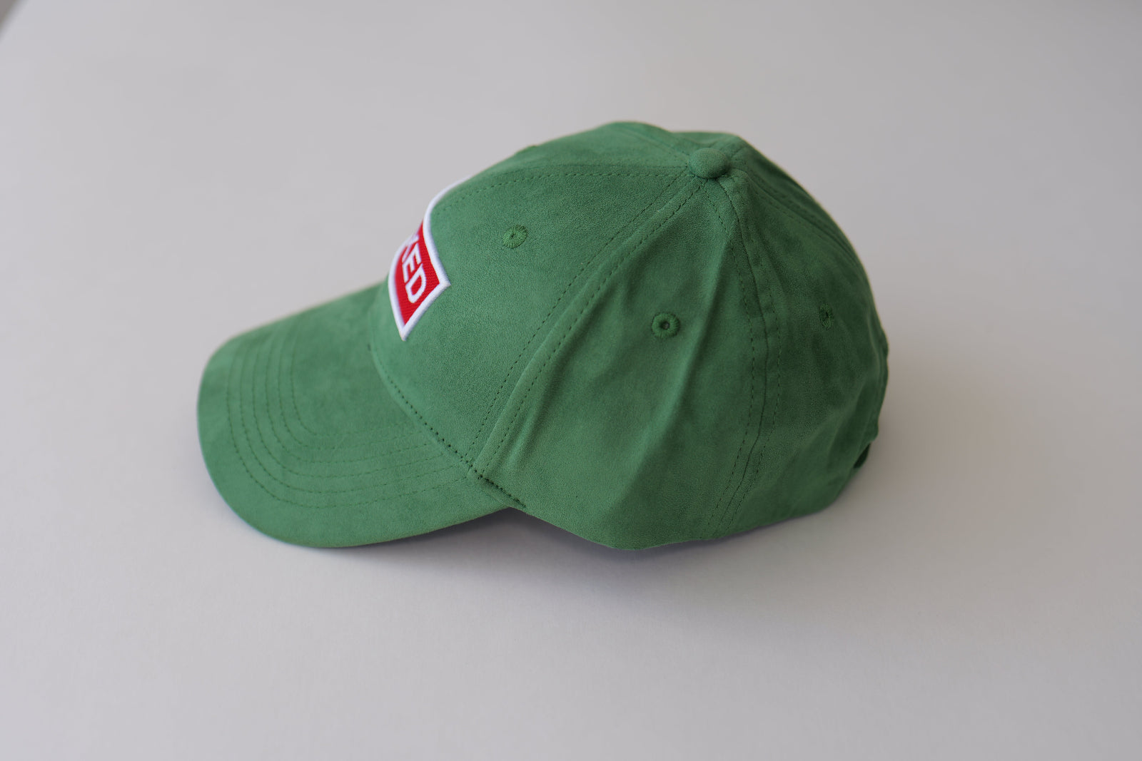 Side studio view of the bABP Signature Collection green eco-suede hat with a red "MIXED" patch, showing the premium textured fabric and curved brim