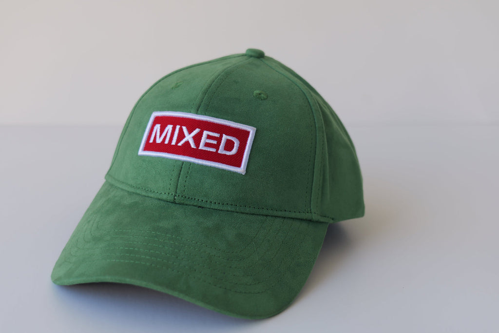 Studio shot of the bABP Signature Collection green eco-suede hat featuring a red and white "MIXED" embroidered patch on a premium textured emerald background