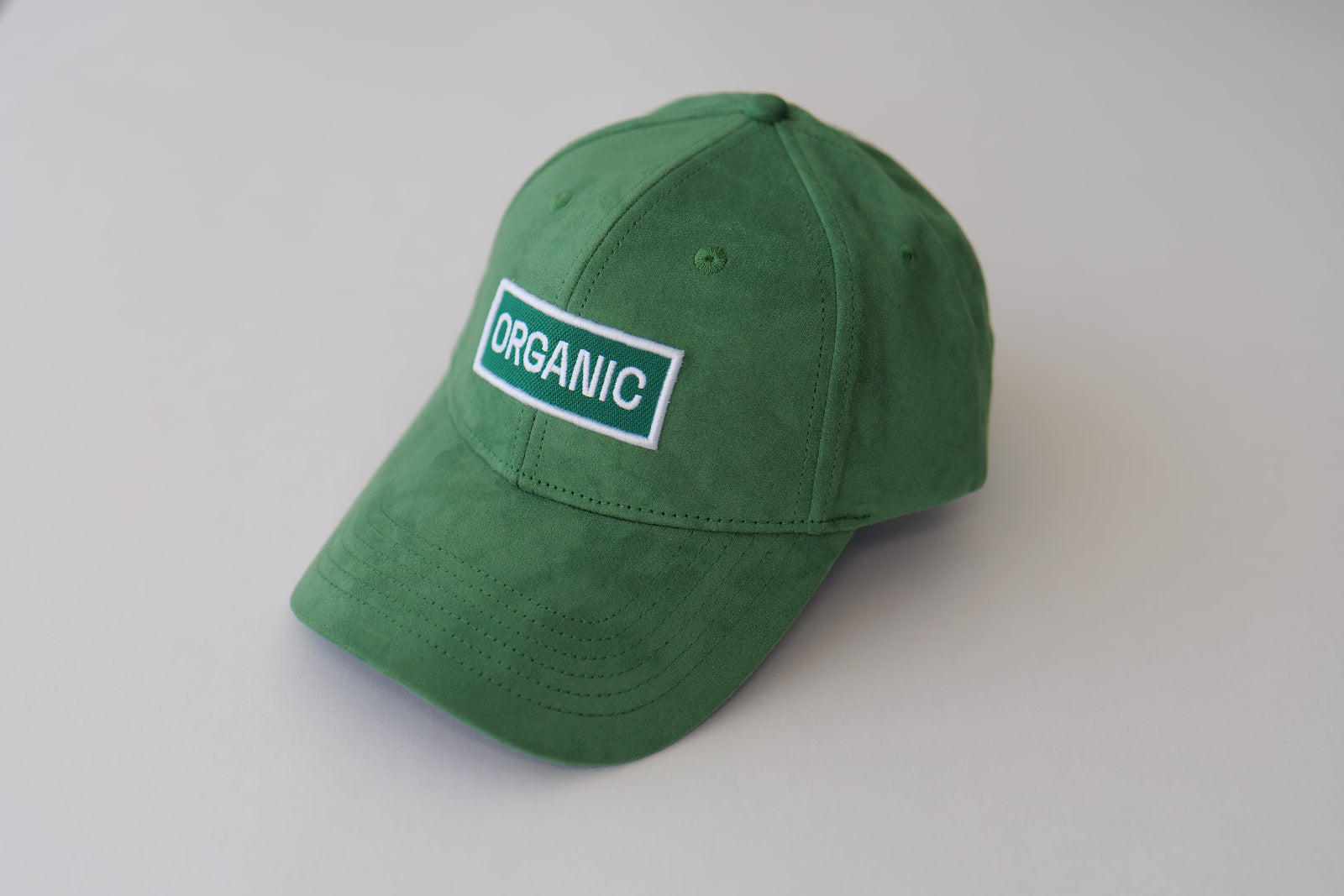 Angled studio shot of the bABP Signature Collection green eco-suede hat with a white "ORGANIC" patch, showcasing the premium fabric texture and structured design
