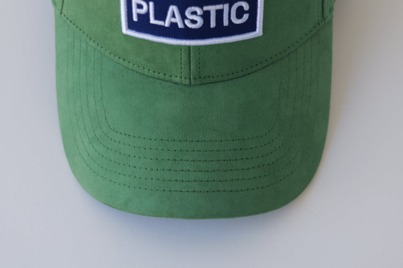 Extreme close-up of the bABP Signature Collection green eco-suede hat featuring a white "PLASTIC" embroidered patch and premium fabric texture