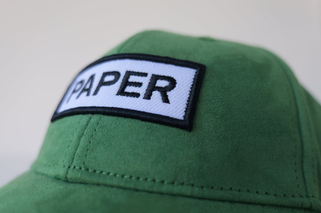 Close-up front view of the bABP Signature Collection green eco-suede hat featuring a white embroidered patch with black "PAPER" text and premium fabric texture