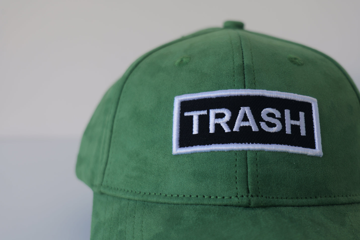 Close-up front view of the bABP Signature Collection green eco-suede hat with a white and black "TRASH" embroidered patch