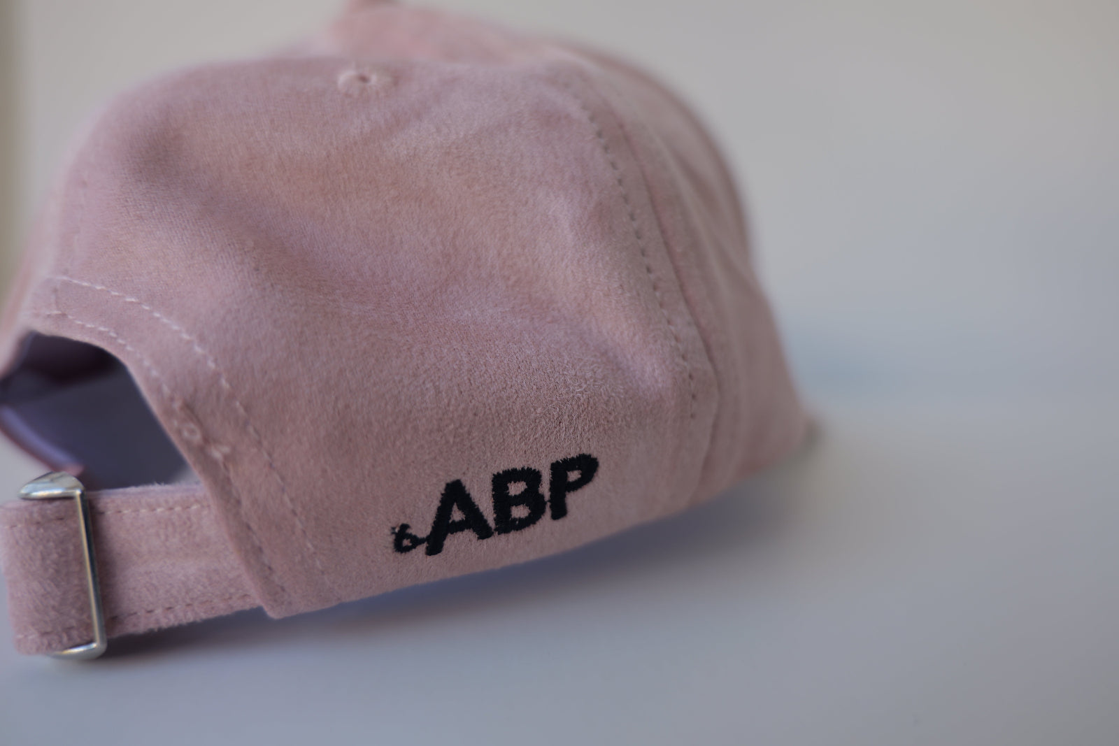 Rear side view of the bABP Signature Collection pink eco-suede hat showing the black "bABP" logo embroidery and the adjustable strap with a metal buckle