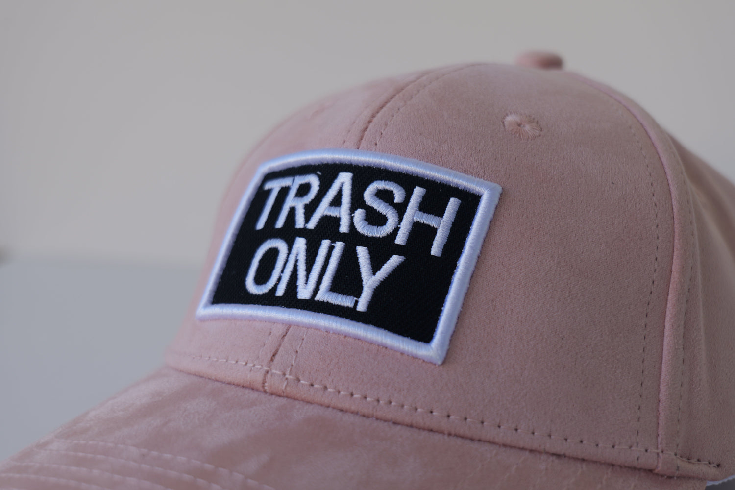 Angled close-up of the bABP Signature Collection pink eco-suede hat featuring the iconic "TRASH ONLY" embroidered logo patch and premium soft fabric texture