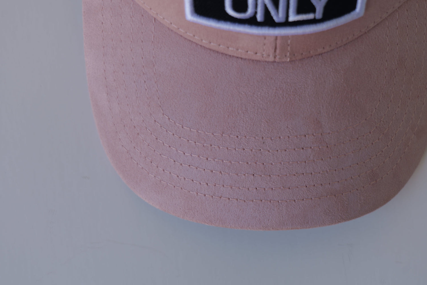 Extreme close-up of the bABP Signature Collection pink eco-suede hat featuring the white and black "TRASH ONLY" embroidered logo patch and premium fabric texture