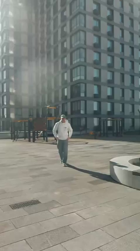 A man in a grey Stussy hoodie putting on a bABP "TRASH" green eco-suede hat, Signature line, with a modern city building in the background and other styles from the collection in the end of the video